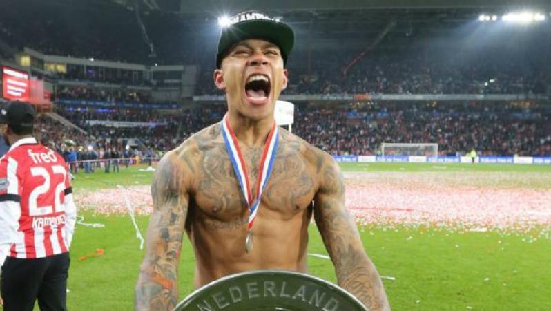 A shirtless Memphis Depay yells in celebration while holding the Eredivisie trophy. 