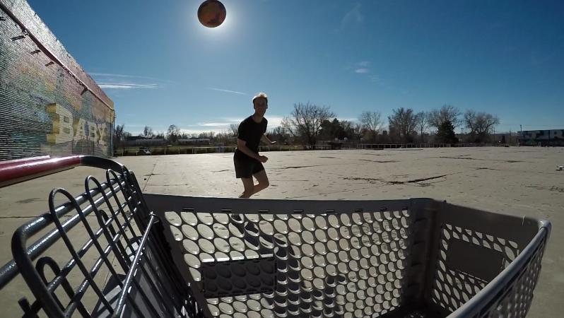 A small tattooed boy heads a soccer ball past the sun as it eclipses into a shopping cart