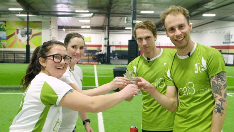 Four contestants hold up shots as they cheers
