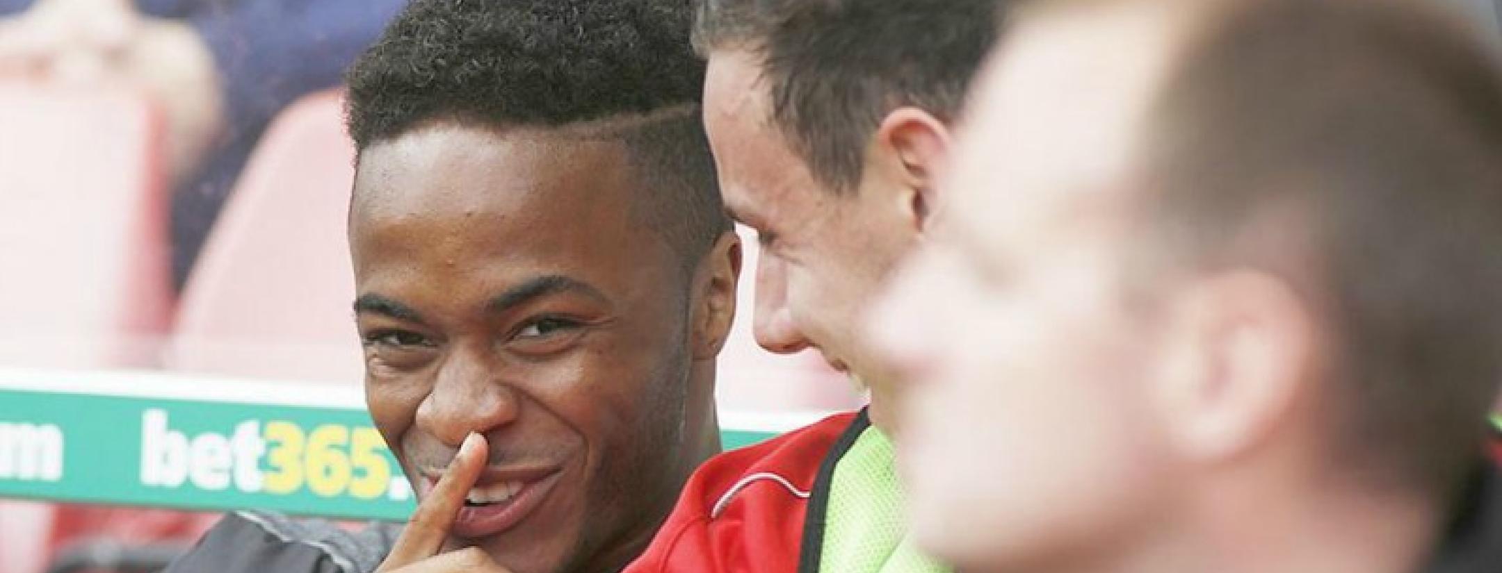 Raheem Sterling is picutred laughing naughtily with his finger to his mouth as if to say "shhh."