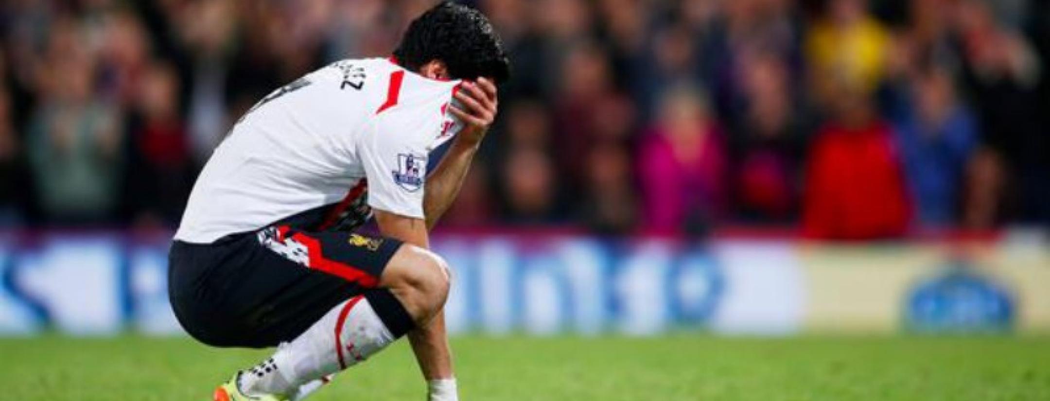 Luis Suarez crouches on the ground, jersey over his face 