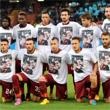 The players all line up for the pregame photo wearing T-Shirts with the first picture of the two fans who died emblazoned on them. 
